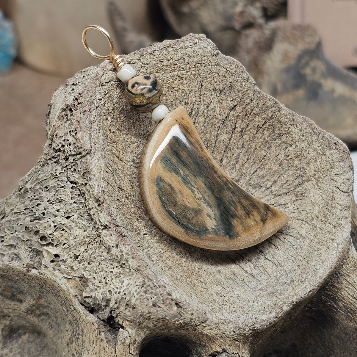 Crescent moon mammoth fossil ivory pendant with dark streaks and a leopard-skin jasper bead, crafted by Kristin R Park at Ice Age Treasures.