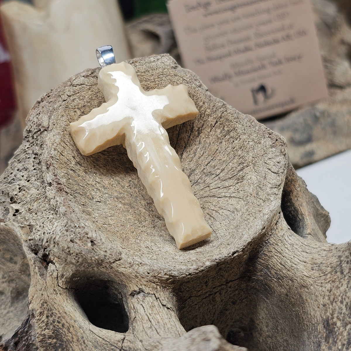 Carved Woolly Mammoth fossil ivory Christian cross pendant with a sterling silver bale displayed on bone, crafted by Kristin R Park at Ice Age Treasures