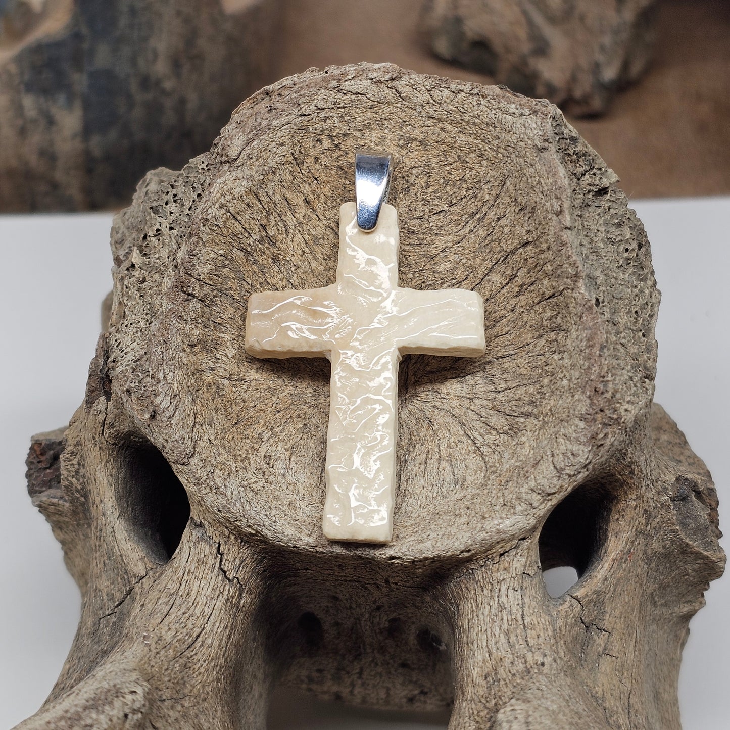 Hand carved woolly mammoth fossil ivory Christian cross pendant with sterling silver bale, displayed on mammoth bone — crafted by Kristin Reeves Park at Ice Age Treasures